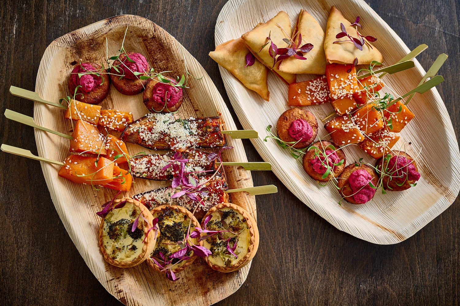 Image displays a range of food offered by Eden Caterers on wooden boards. Including samosas, canapés, and quiches.