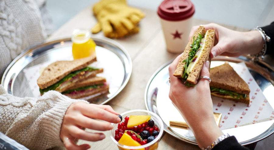 Two people eating lunch at Pret, including sandwiches, fruit, orange juice, and coffee