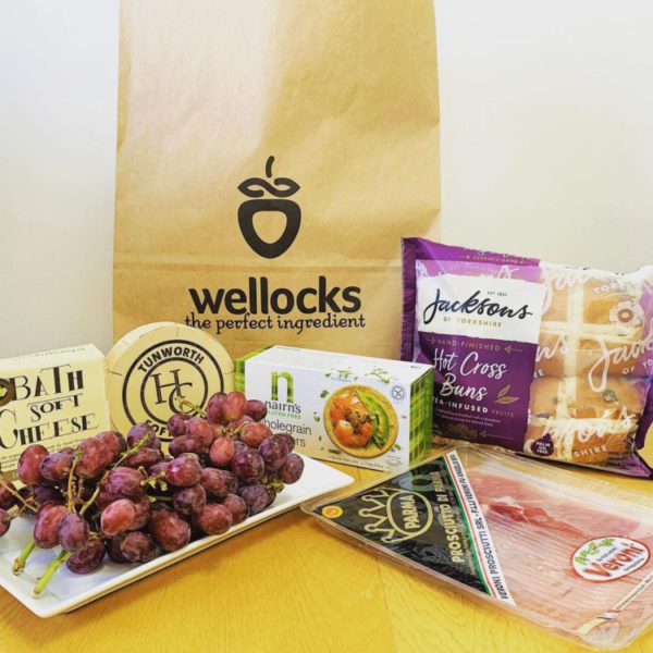 Display of Wellock produce, including grapes, proscuitto, cheese, and hot cross buns